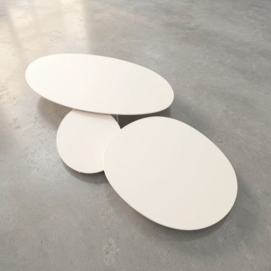A set of three Pebbles - Coffee Tables by TIBA-TIBA in various sizes. The tops of the tables are Dekton - Aeris in an off-white colour, and the tables are nesting as they are arranged on a grey concrete floor.