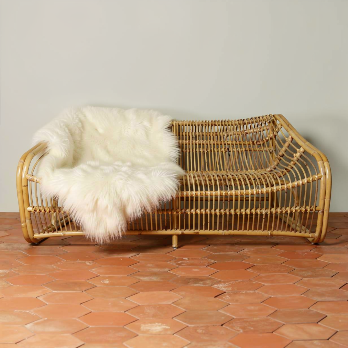 Bucket 2-Seater Sofa by TIBA-TIBA – unique rattan sofa with sweeping curved frame on terracotta hexagonal tiles and a sheepskin draping over the back.