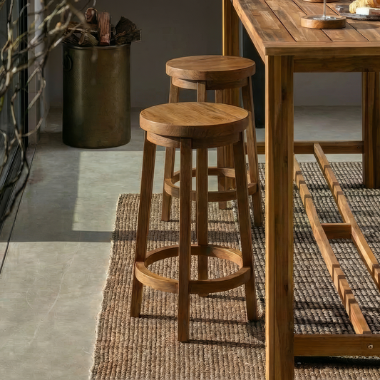 Three Sixty Stools by TIBA-TIBA – warm interior with two handcrafted round teak wood bar stools with rotating seat at teak bar table on brown woven lotus leaf rug.