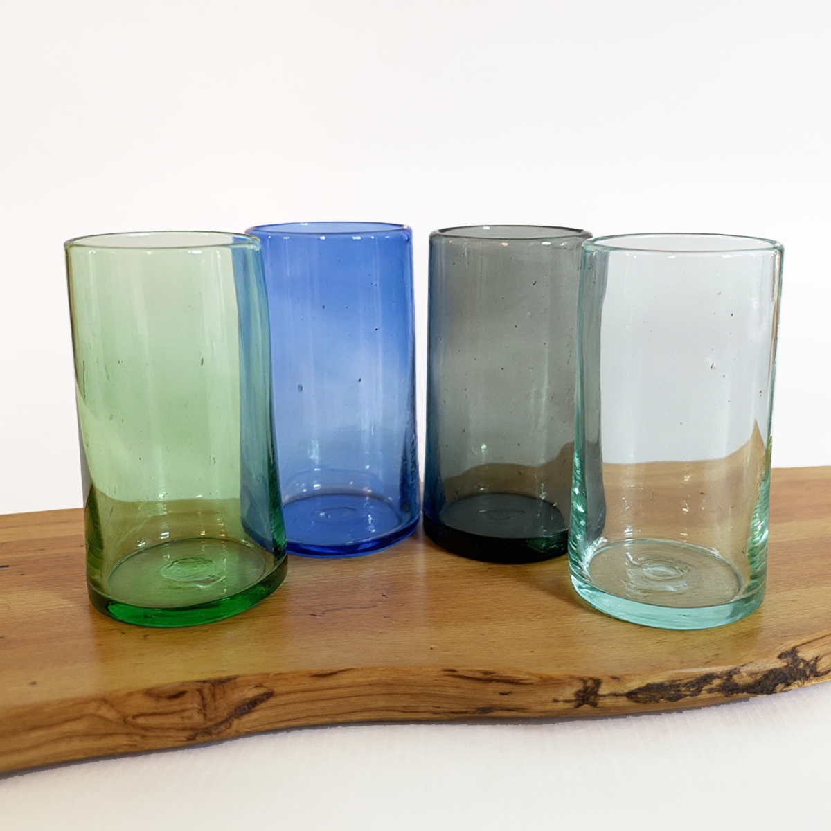 Four coloured glass Tube Tall Tumblers by TIBA-TIBA – Hand blown, recycled green, blue, smoke grey and naturally clear tall cocktail glasses on Teak wood. 