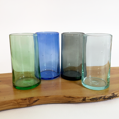 Four coloured glass Tube Tall Tumblers by TIBA-TIBA – Hand blown, recycled green, blue, smoke grey and naturally clear tall cocktail glasses on Teak wood. 