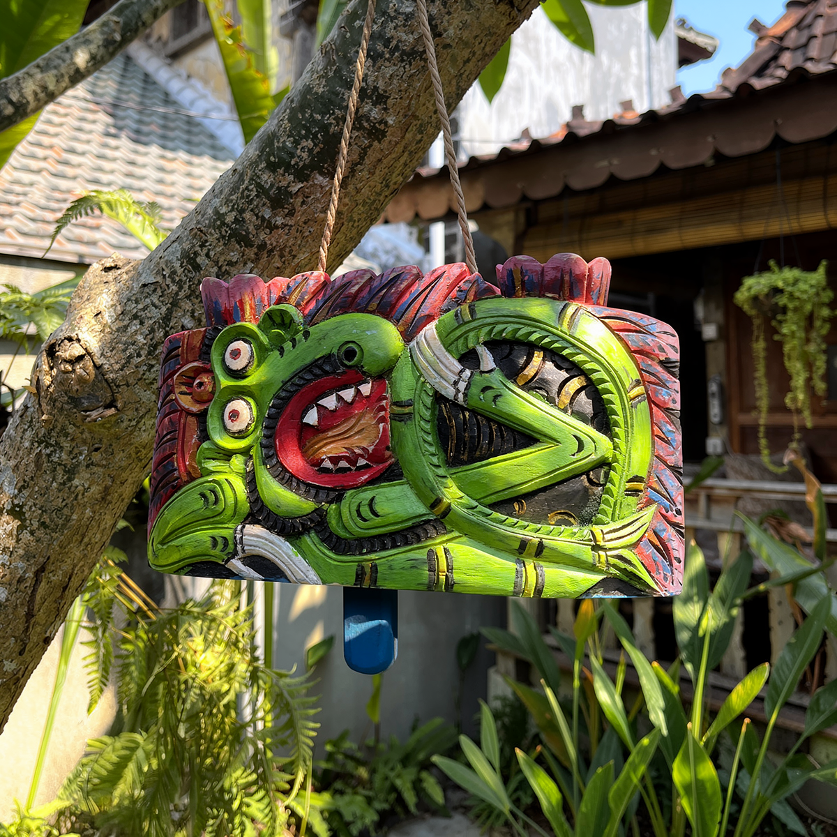 Lonceng Sapi Cowbell by TIBA-TIBA – 
Solid Mahogany Bali cowbell with green dragon design hanging from a frangipani tree in front of a Joglo 