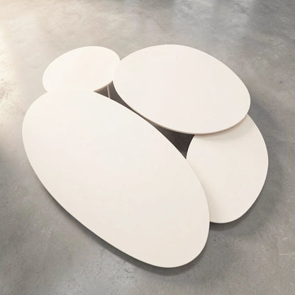 A set of four modern oval-shaped  Pebbles - Coffee Tables in Various sizes by TIBA-TIBA. The tables have a Dekton top in an off-white finish, and are nesting and overlapping each other as they are arranged on a grey concrete floor
