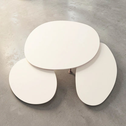A set of three Pebbles - Coffee Tables by TIBA-TIBA in various sizes. The tables have a Dekton top in an off-white finish, and are nesting and overlapping each other. They are arranged on a grey concrete floor.