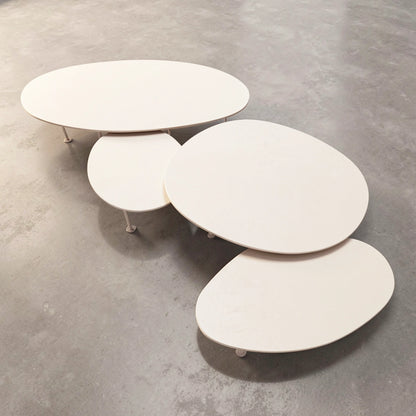 A set of four nested, organic-shaped Pebbles - Coffee Tables by TIBA-TIBA in a warm off-white finish of Dekton Aeris, resting on a textured grey concrete floor.