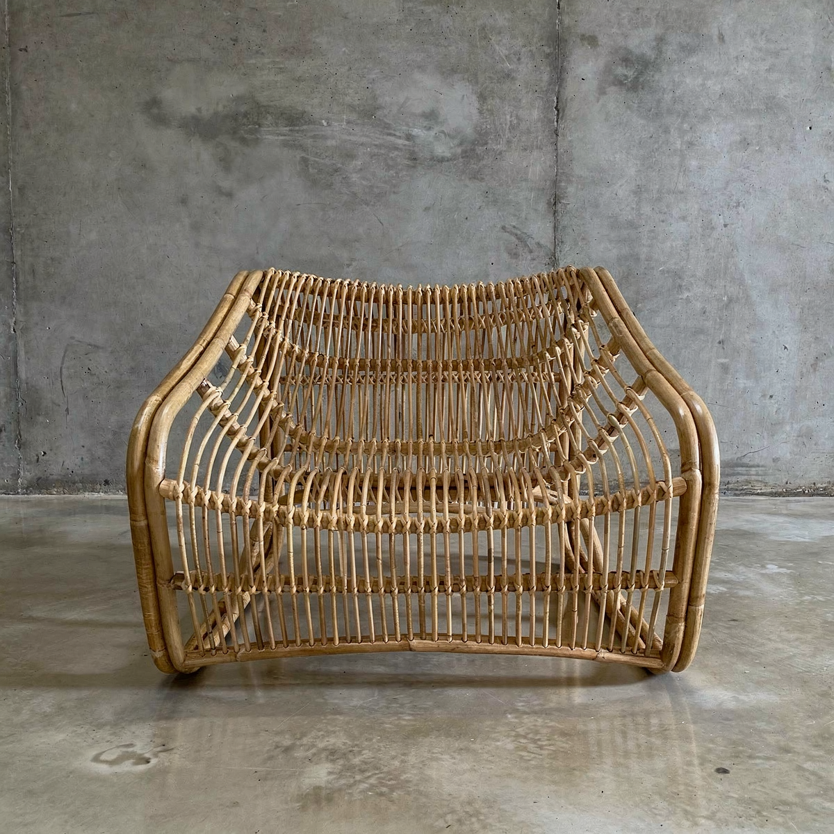 Bucket Lounge Chair by TIBA-TIBA -Modern handmade Indonesian rattan bucket chair on polished concrete floor with concrete wall background. 