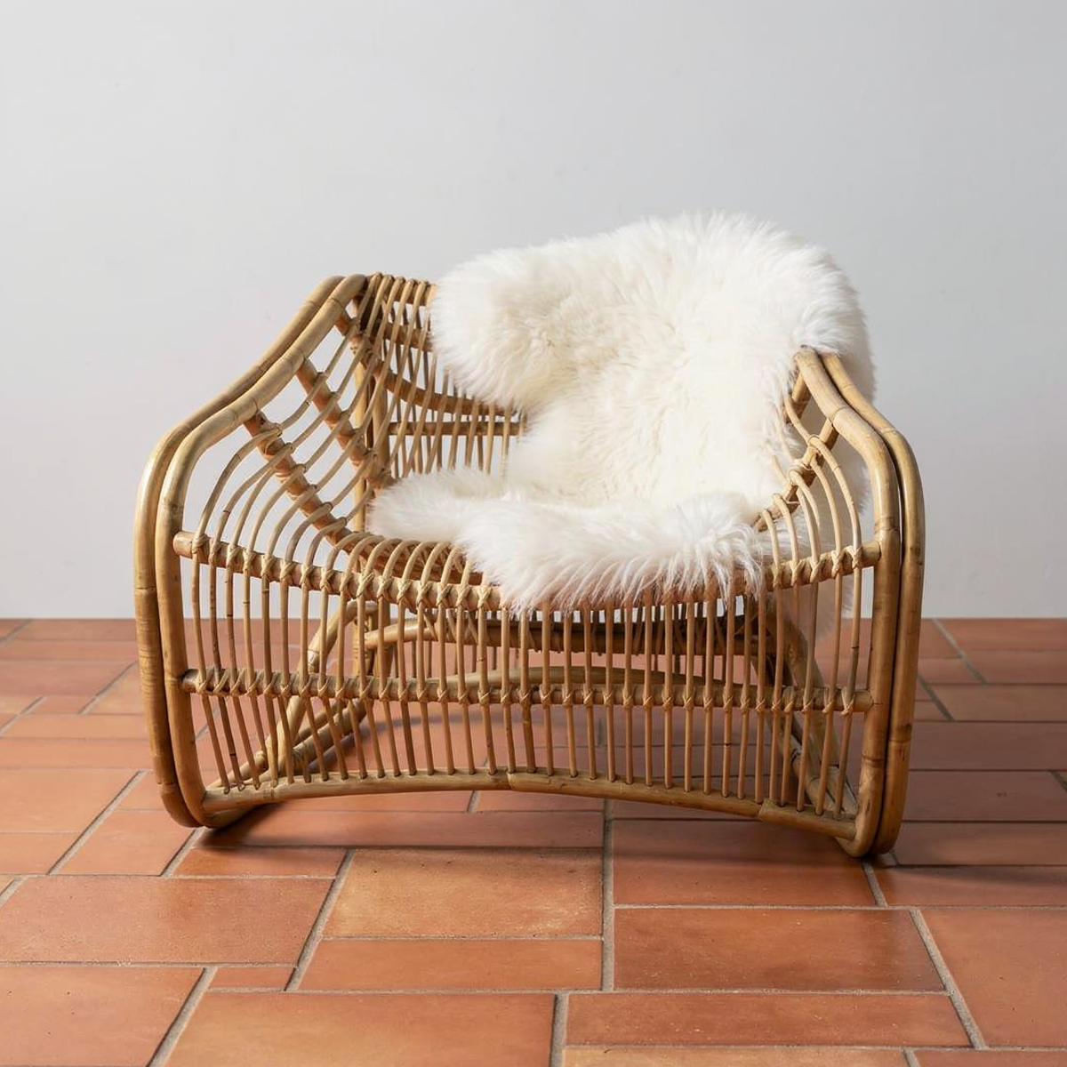 Bucket Lounge Chair by TIBA-TIBA -Modern rattan bucket lounge chair on polished red brick floor with sheepskin draping over back of chair