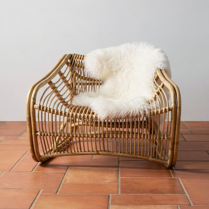 Bucket Lounge Chair by TIBA-TIBA -Modern rattan bucket lounge chair on polished red brick floor with sheepskin draping over back of chair