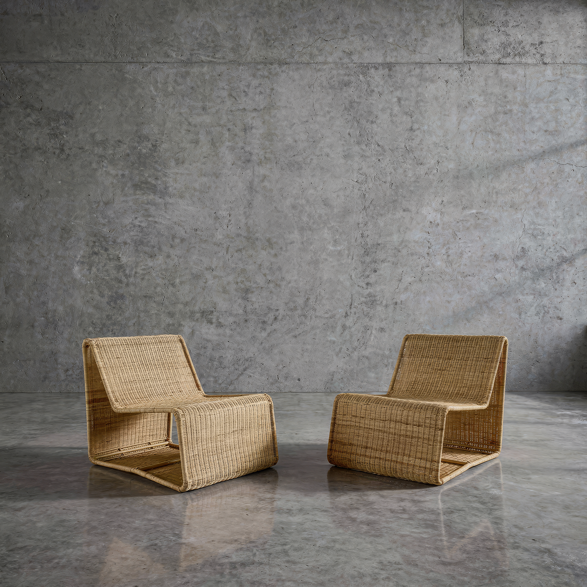 Geo Lounge Chair by TIBA-TIBA – Two handwoven minimalist rattan lounge chairs on polished concrete floor and concrete wall background. 