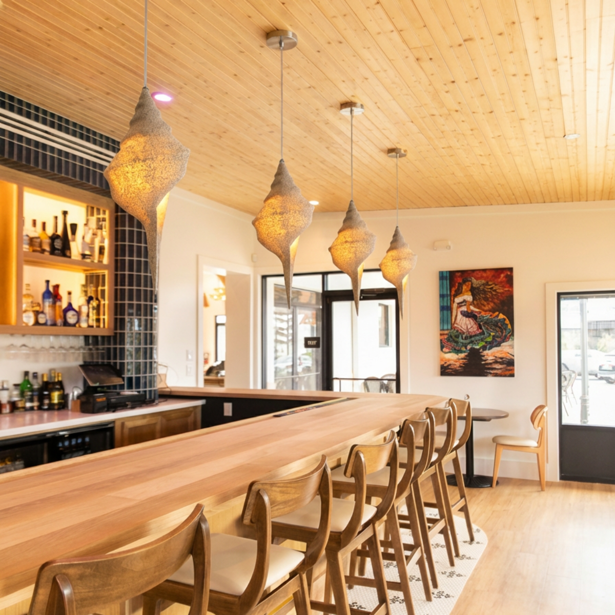 Keong Pendant Light by TIBA-TIBA - series of sand coated resin shell pendant lamps hanging over a warm, minimalist wooden restaurant bar. 