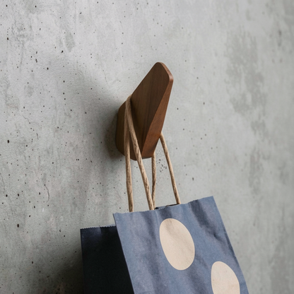 Fin Wall Hook by TIBA-TIBA - Sculptural wooden wall hook mounted on a concrete wall with hanging blue polkadot bag.