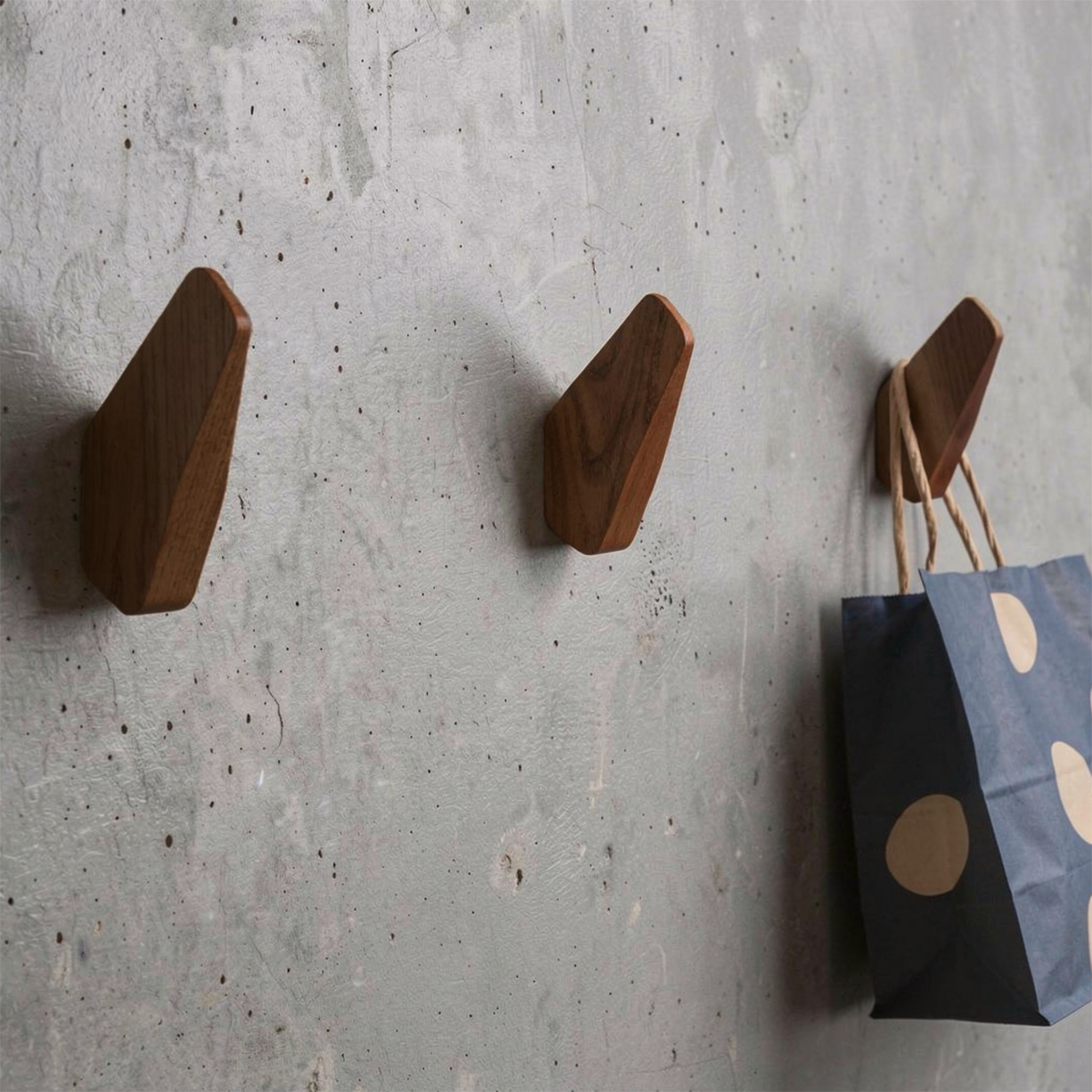 Fin Wall Hook by TIBA-TIBA - Three artistic wooden airplane fin wall hooks mounted on a concrete wall with blue polkadot bag hanging from one hook.  