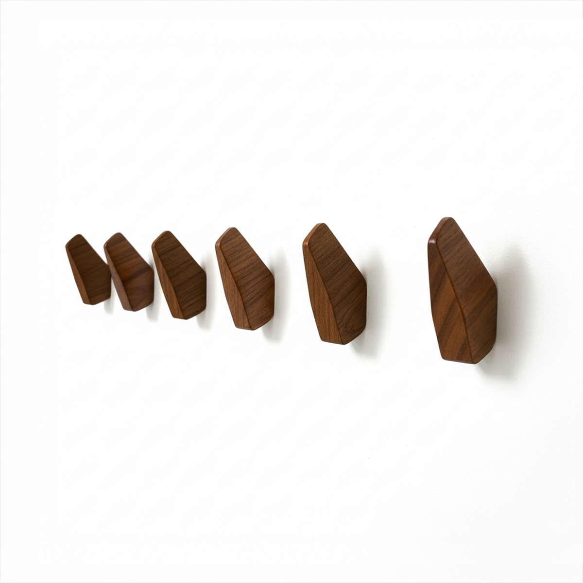 Fin Wall Hook by TIBA-TIBA -  Row of six sculptural, abstract teak wall hooks mounted on a white wall. 