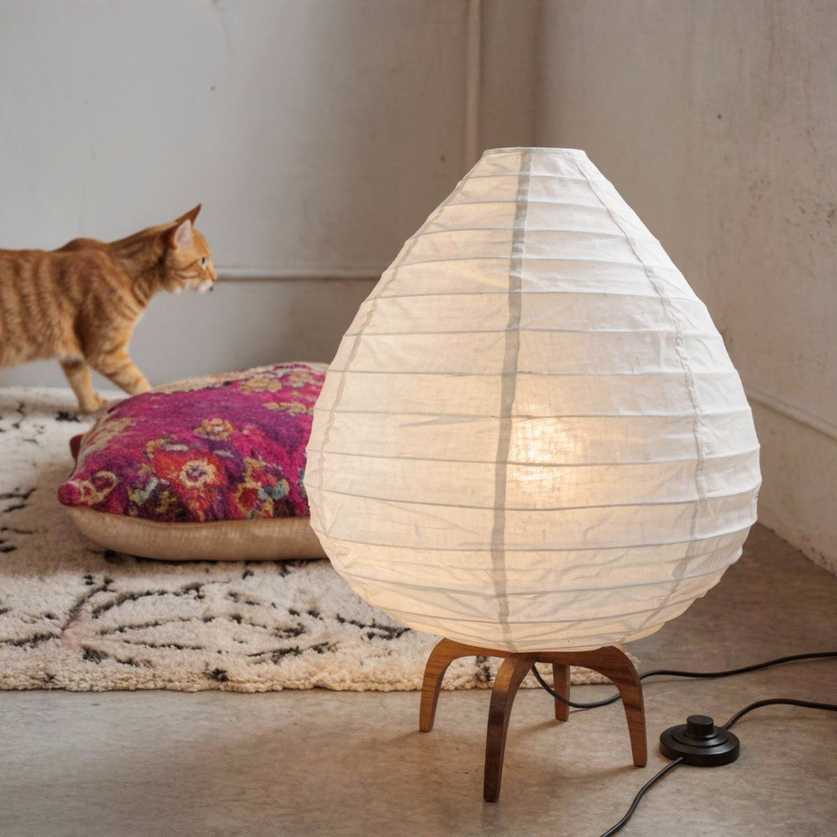 Alien Floor Lamp by TIBA-TIBA – sculptural linen floor light with teak base, styled in a cozy modern living room with textured pillows, natural wood table, and tropical plant.on bohemian rug and pillow with cat in background. 