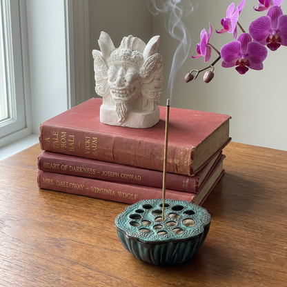 Barong Sculpture by TIBA-TIBA – hand-cast white concrete Balinese Barong paperweight on a stack of books including A Tale From Bali by Vicki Baum, and the Lotus Ashtray with burning incense in foreground. 
