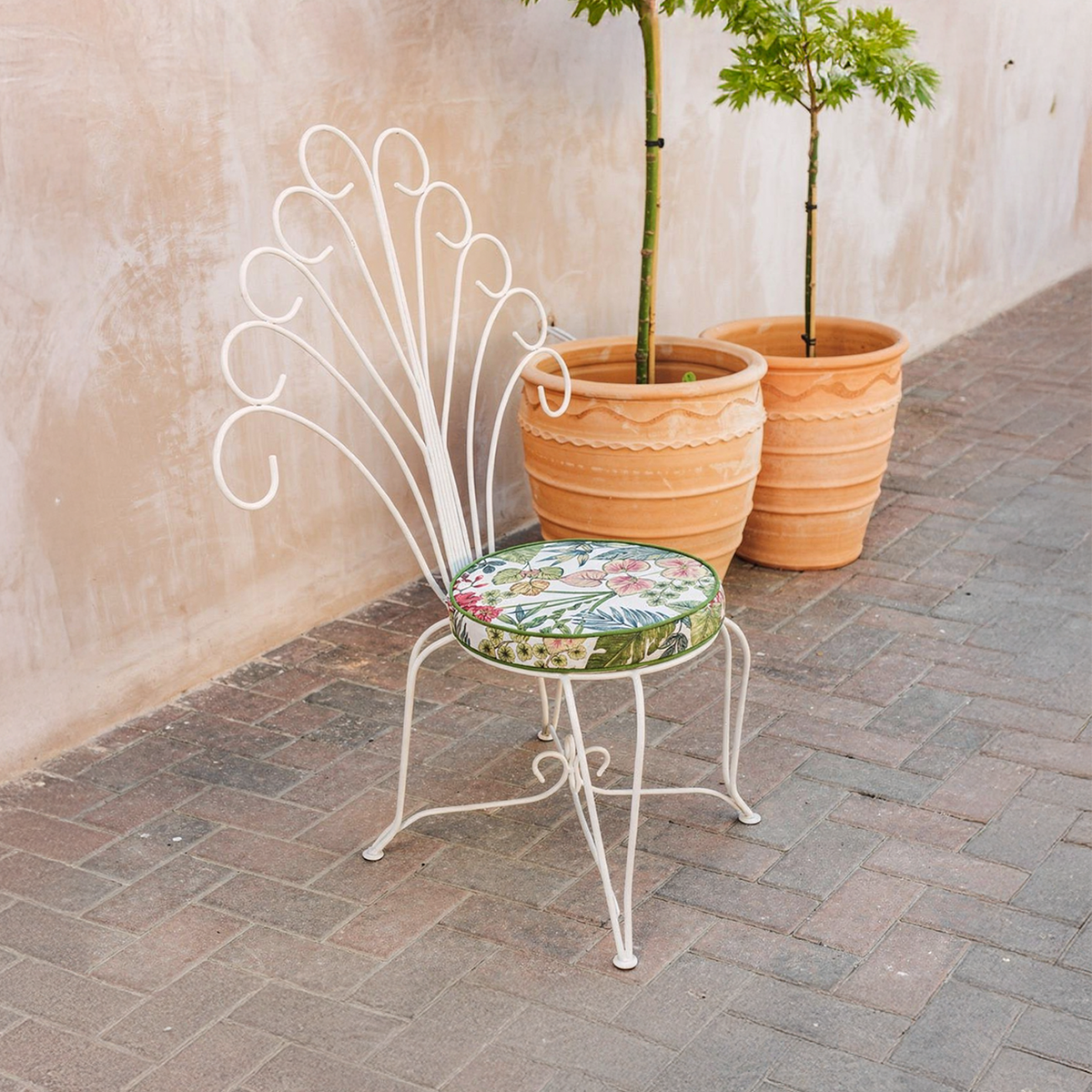 Plume Chair by TIBA-TIBA – white metal peacock chair with decorative curly steel back in terracotta outdoor setting.