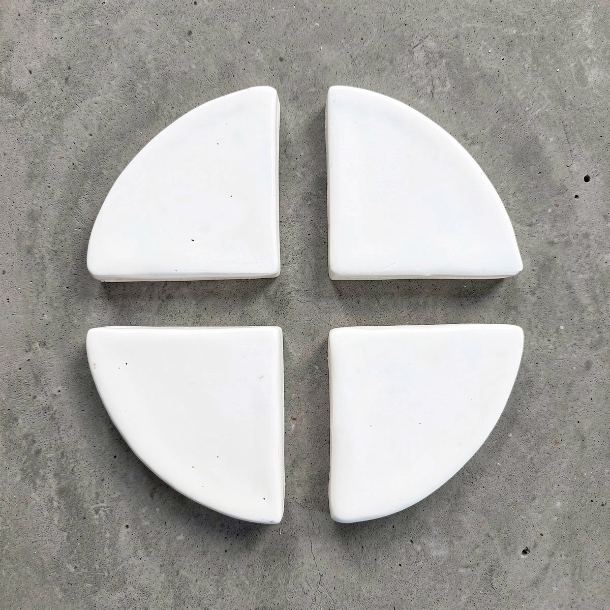 Po-Ka Pot feet by TIBA-TIBA - set of four white glazed ceramic wedges for planter drainage and airflow on concrete background. 