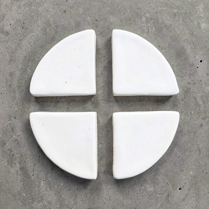 Po-Ka Pot feet by TIBA-TIBA - set of four white glazed ceramic wedges for planter drainage and airflow on concrete background. 